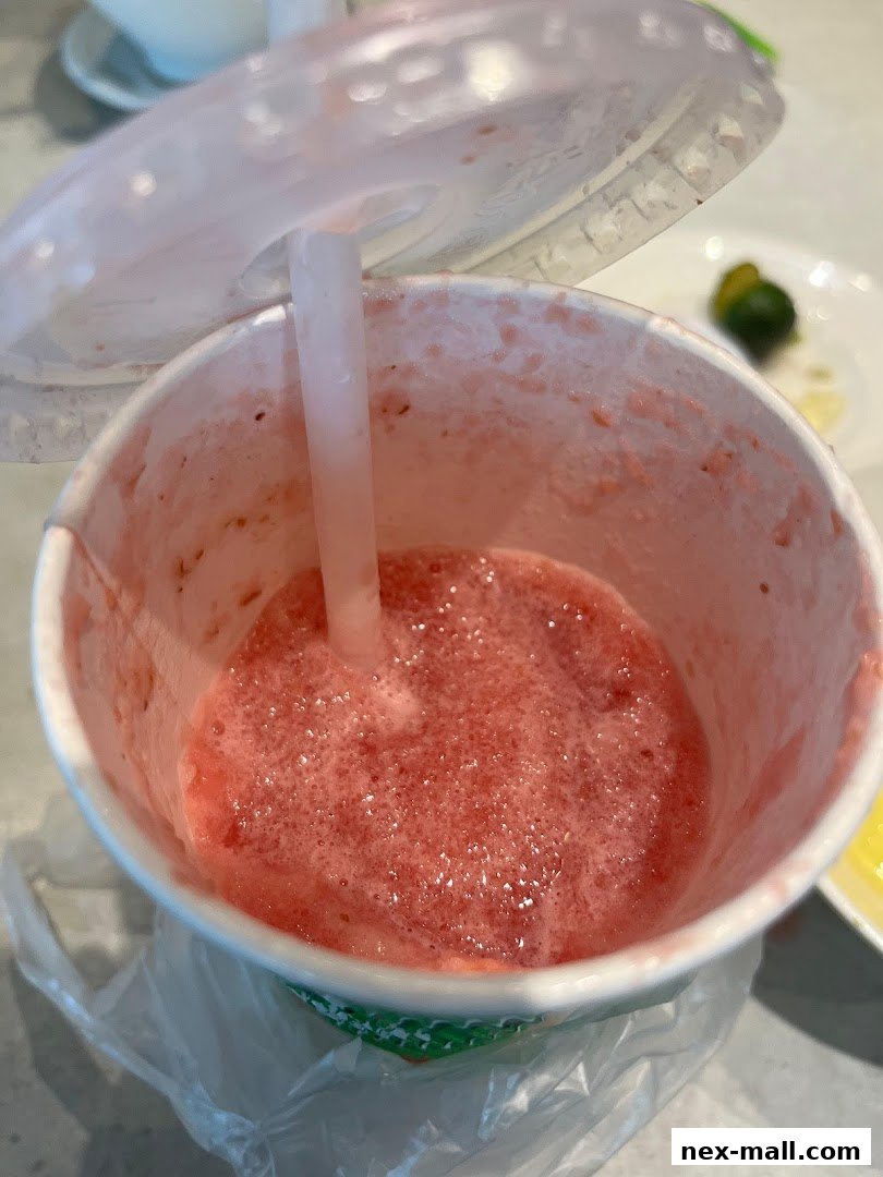 A close-up of a partially consumed strawberry smoothie in a white cup with a straw.