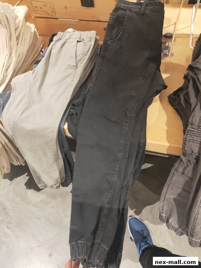 A display of casual pants in various neutral colors, neatly folded on a wooden shelf.