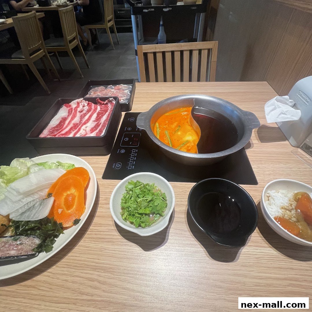 A table set for shabu-shabu with raw meat, vegetables, and a split broth pot.