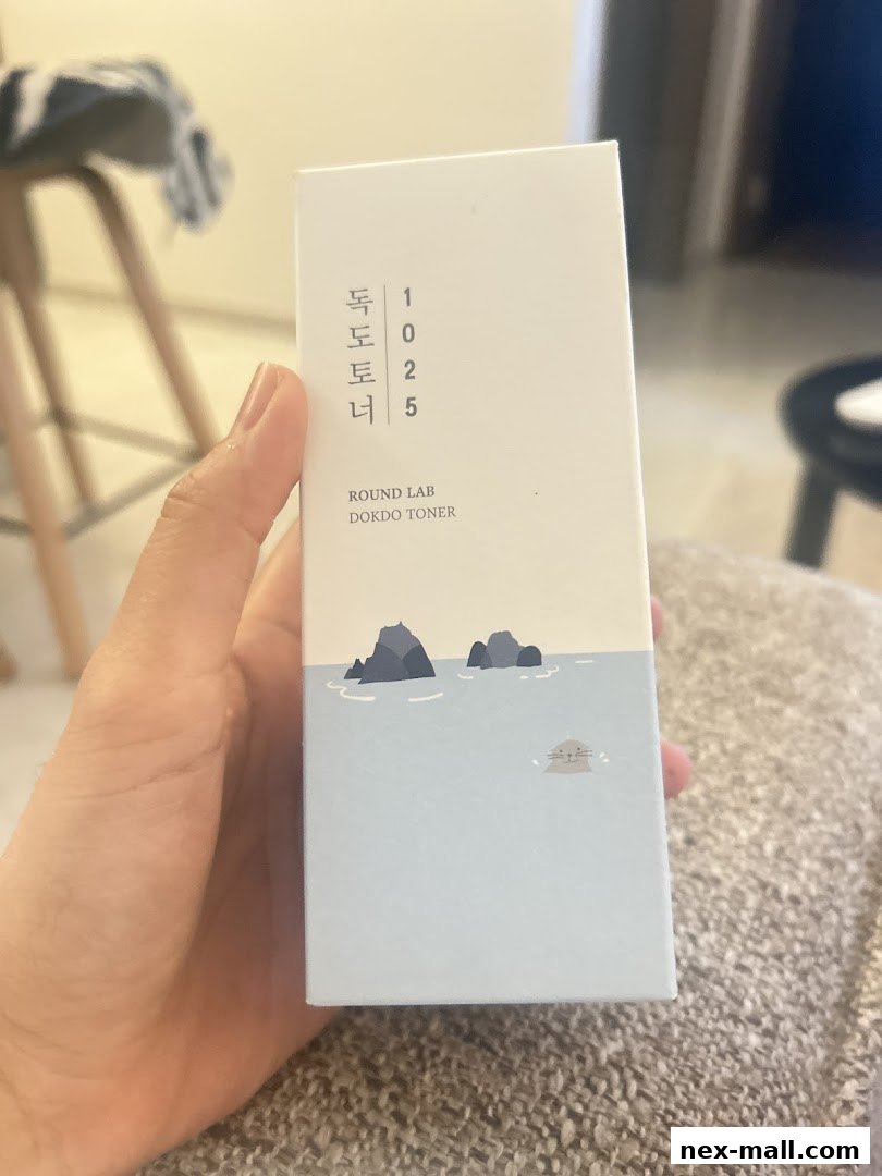 A hand holds a box of Round Lab Dokdo Toner with Korean text and a seal illustration.