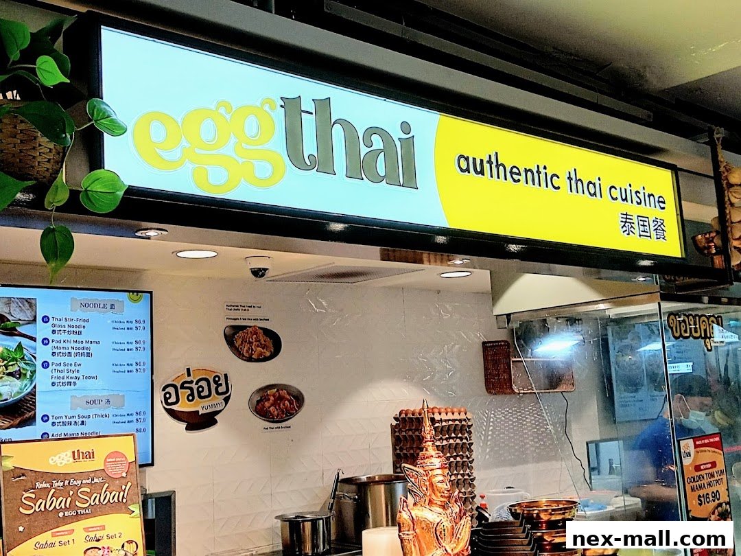 A brightly lit food stall with a prominent sign for 'eggThai' offering authentic Thai cuisine.