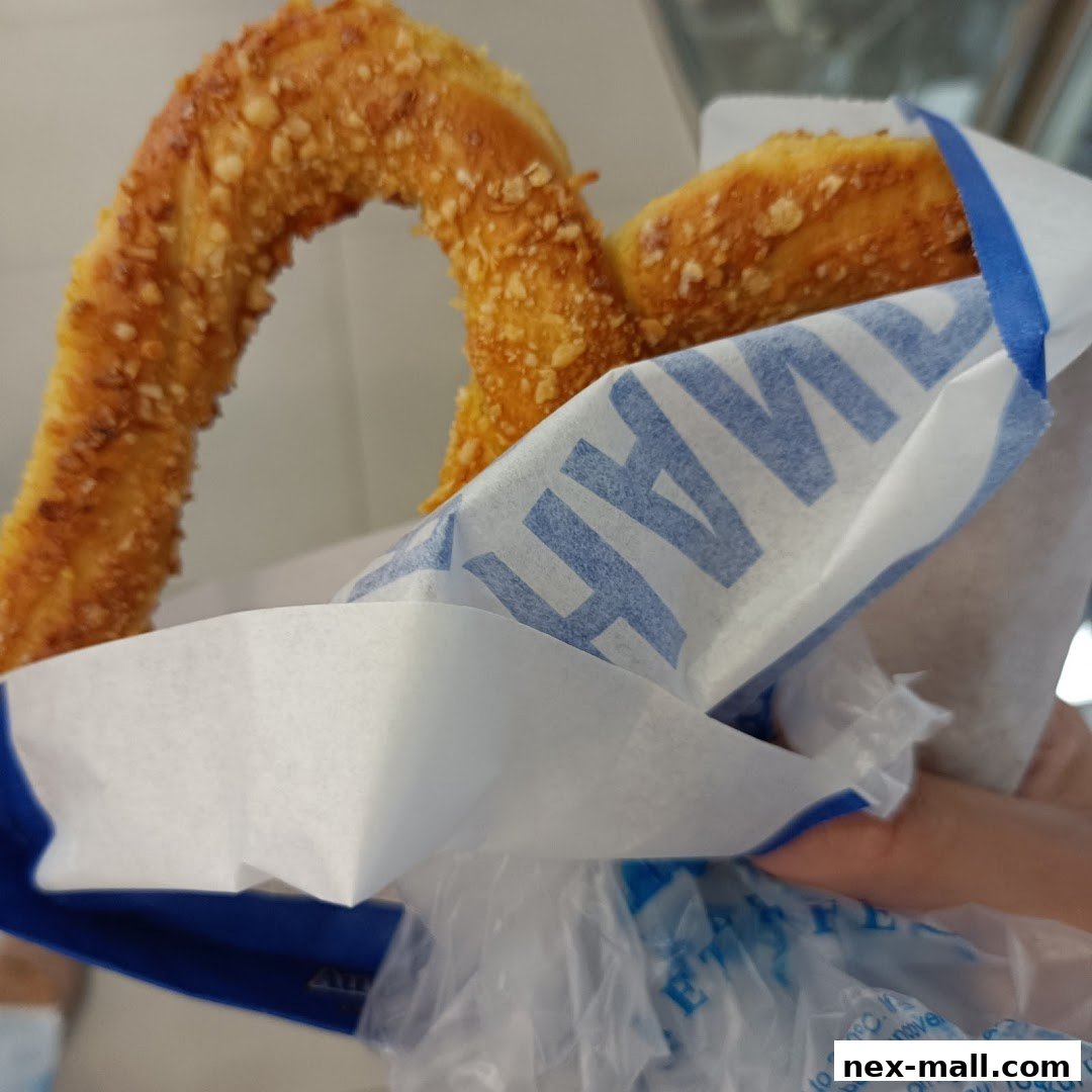 A close-up shot of a freshly baked pretzel with a crunchy topping, held in branded packaging.
