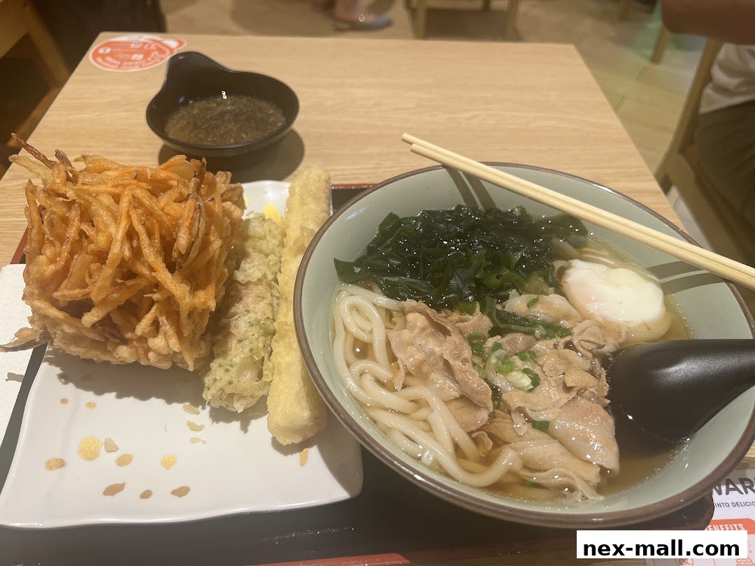 A bowl of udon noodles with tempura and a side of dipping sauce.