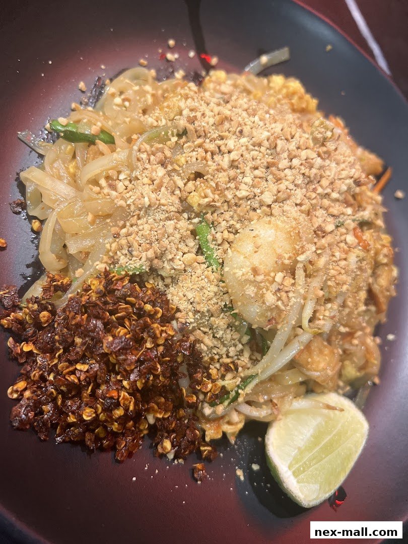 A close-up of a delicious Pad Thai dish with peanuts, chili flakes, and a lime wedge.