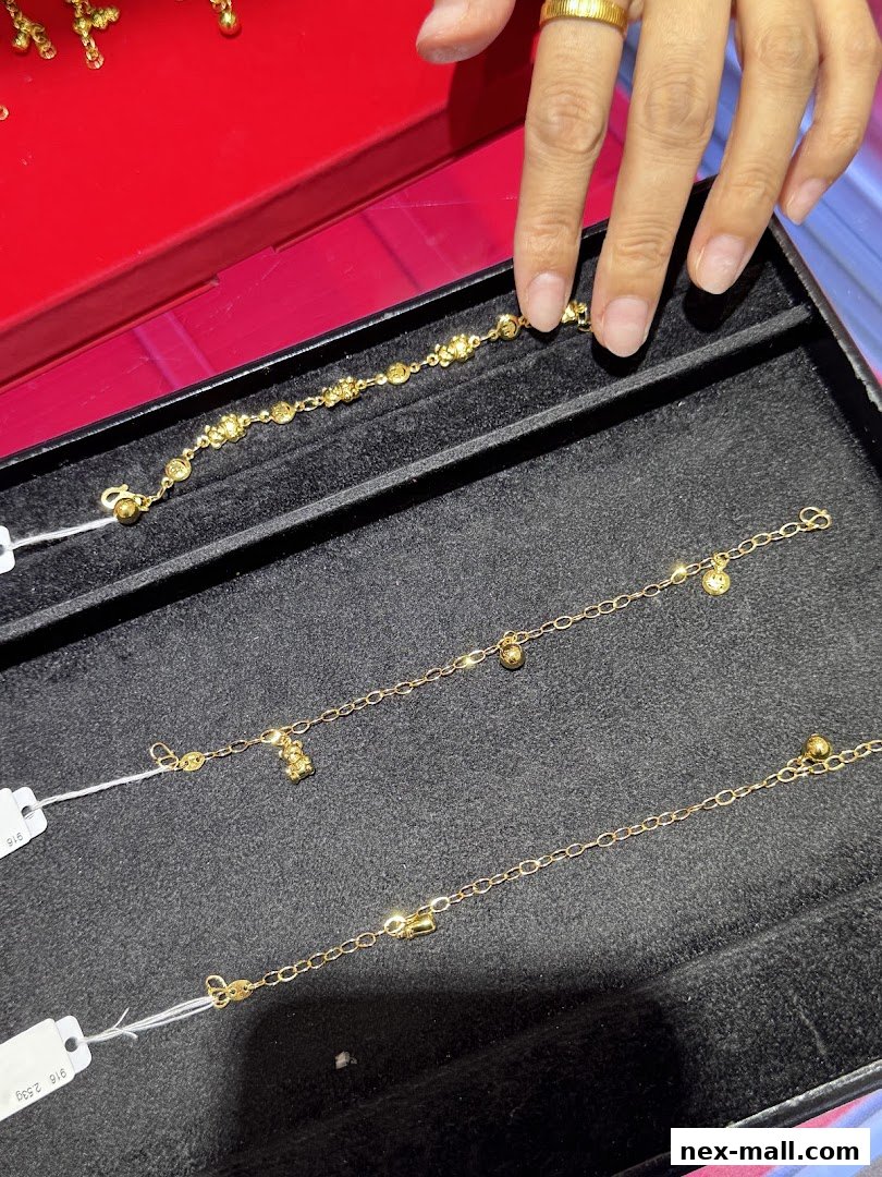 A hand with a gold ring is selecting a delicate gold bracelet from a display.