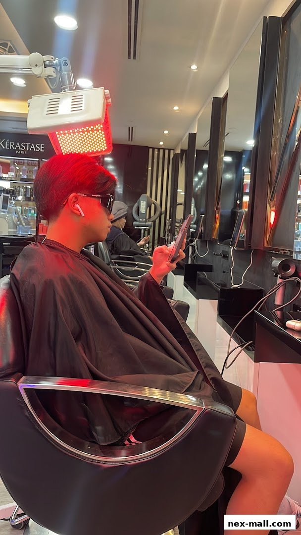 A person sits in a salon chair under a red heat lamp, looking at their phone.