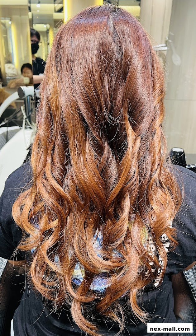 A person's back with long, wavy, reddish-brown hair styled with curls.