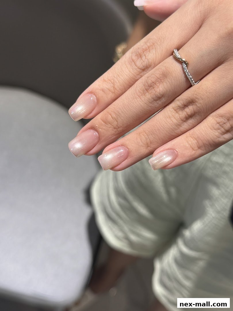 Close-up of a person's hand with a subtle pearlescent manicure and a diamond ring.
