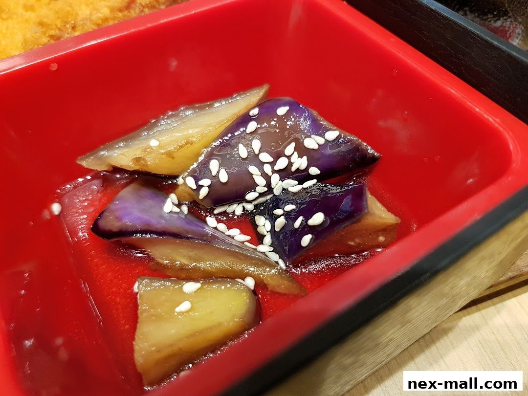 Close-up of glazed eggplant pieces with sesame seeds in a red bento box.