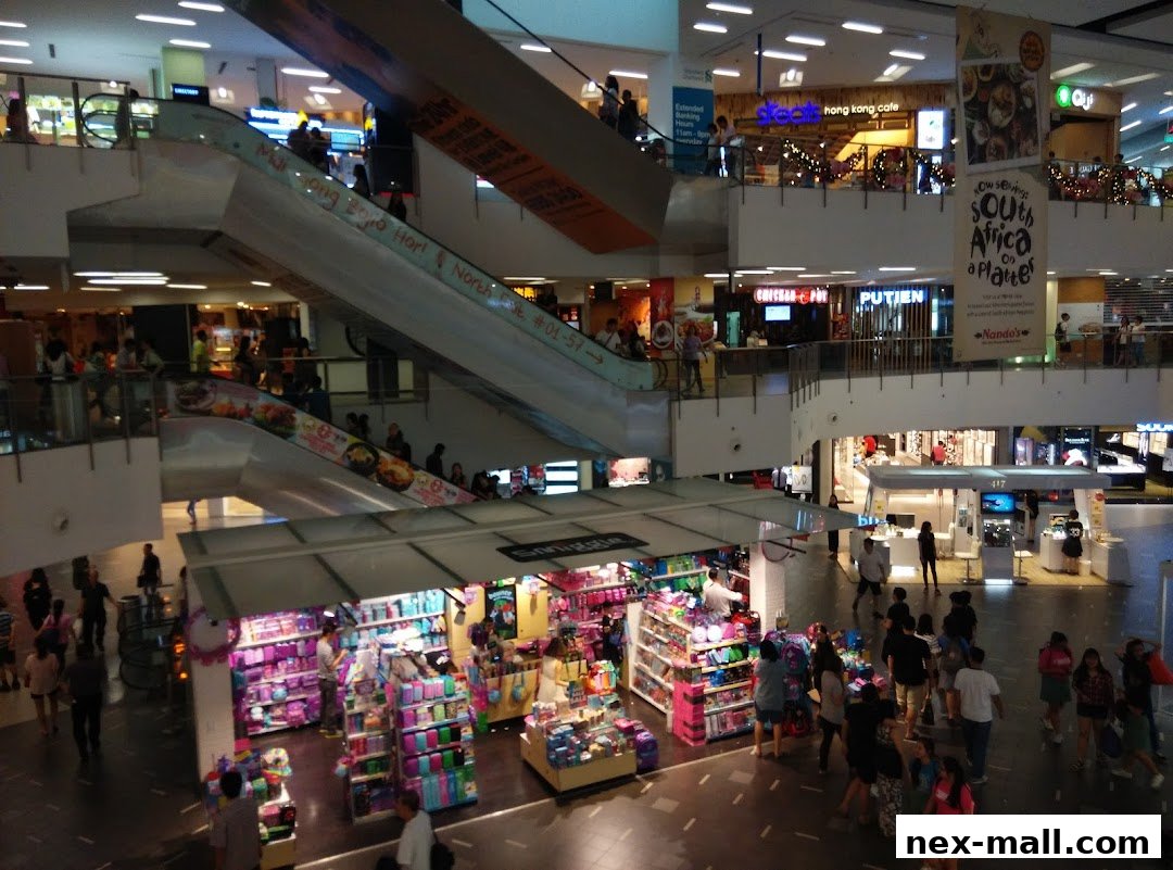 A busy shopping mall interior with escalators, shops, and many shoppers.