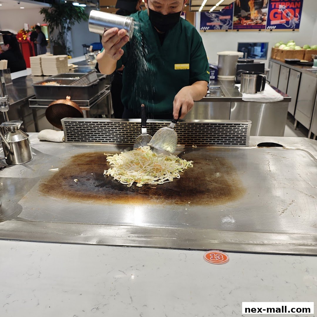 A chef seasons vegetables being cooked on a large flat-top grill.