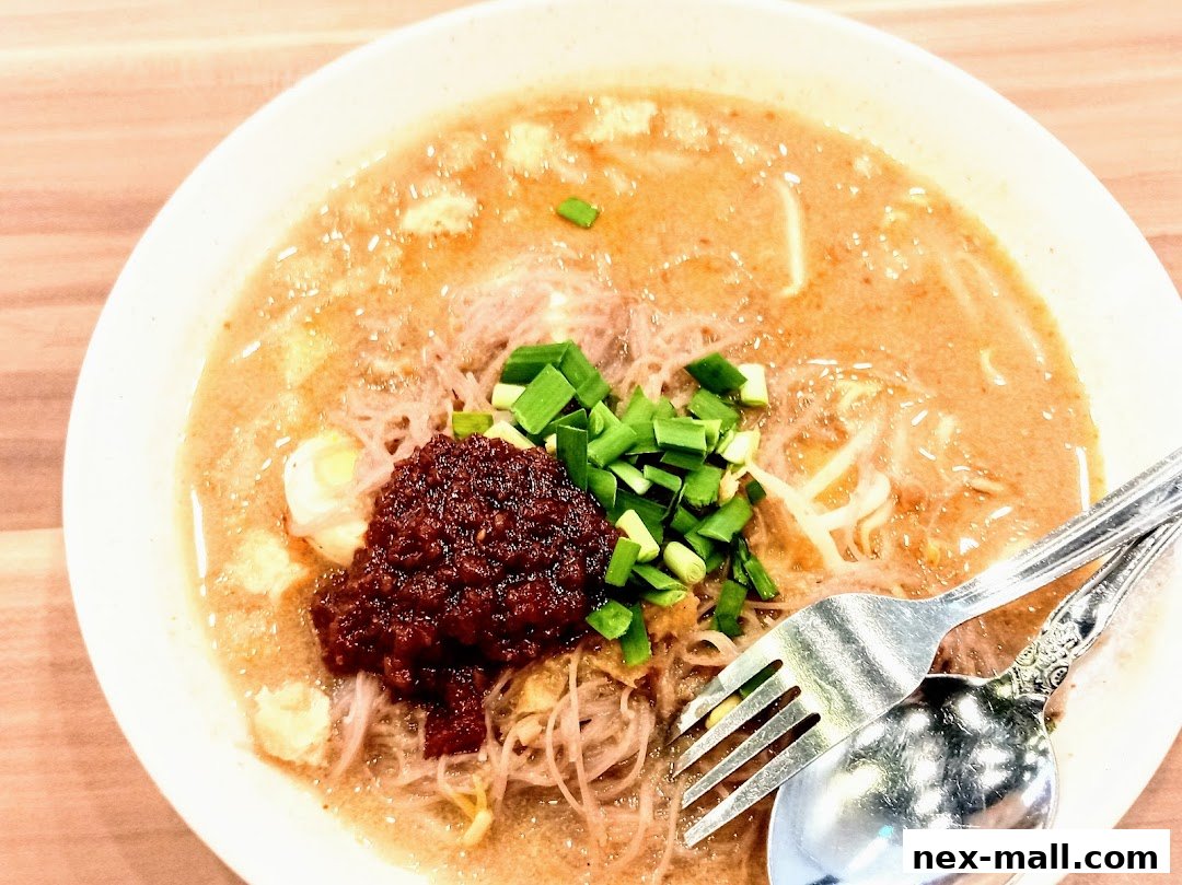 A close-up shot of a bowl of Laksa with chili paste and chopped spring onions.