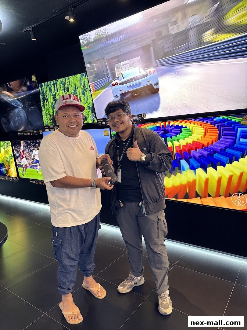Two men smiling in a store with large screens displaying various content.
