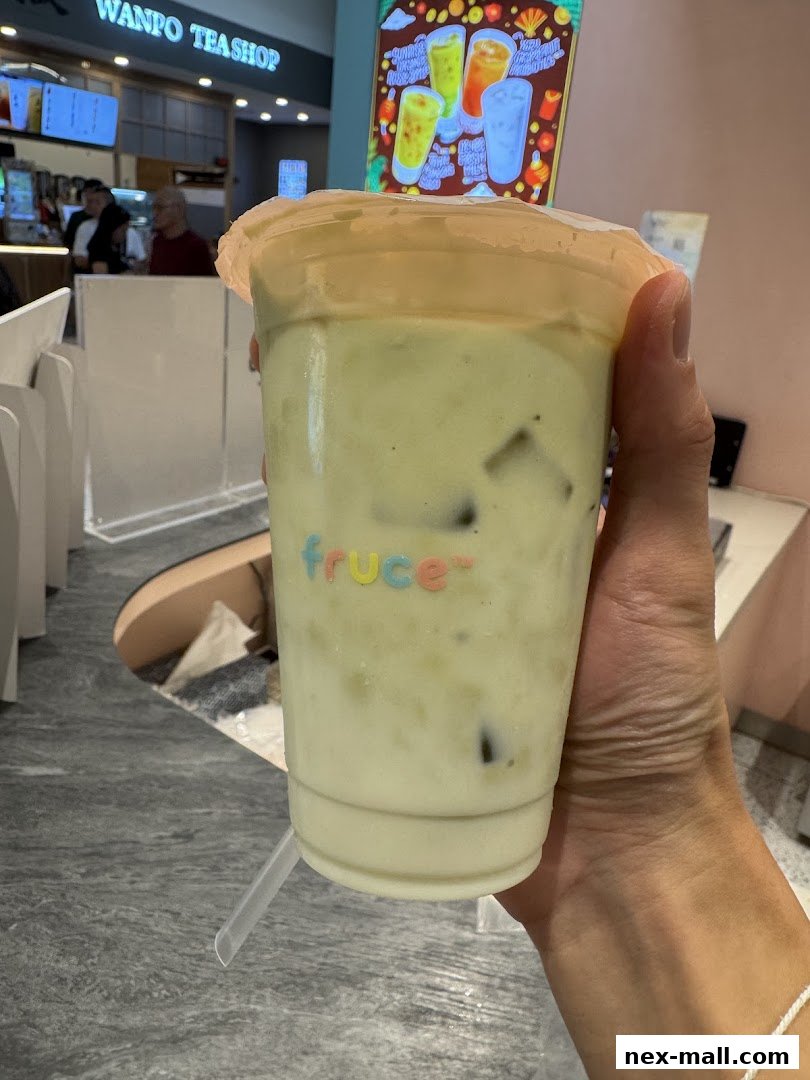 A hand holds a creamy green beverage with ice from Fruce.