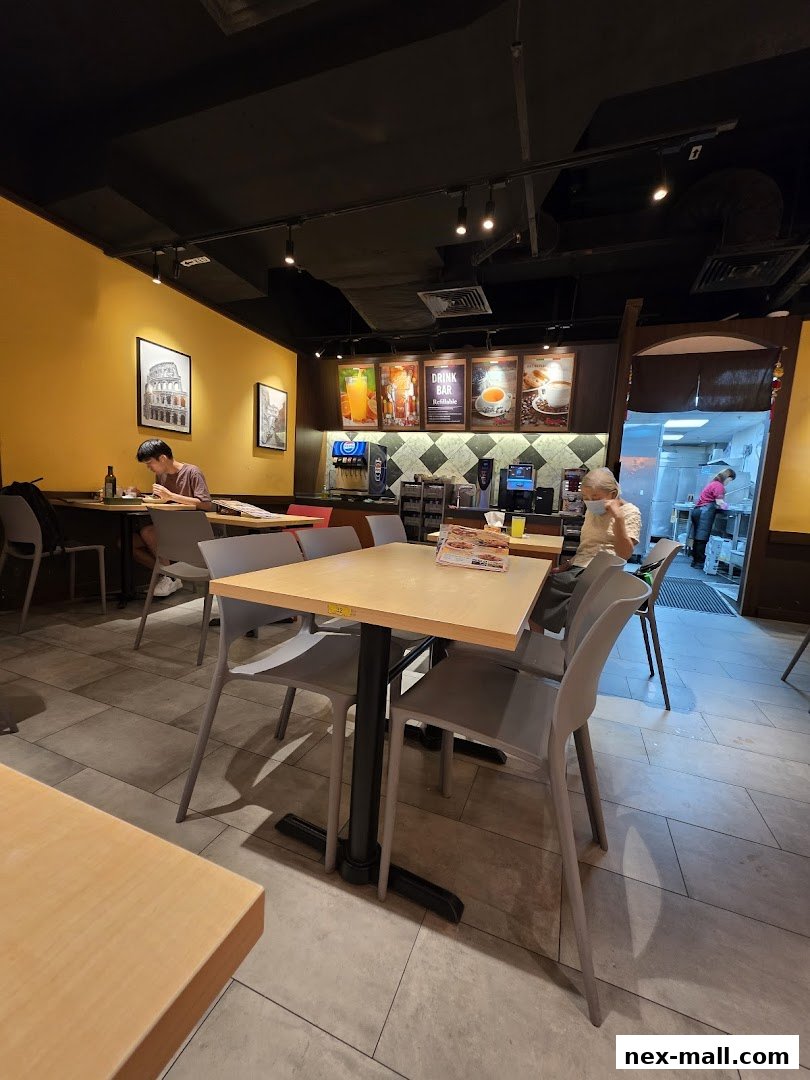 Interior view of a Saizeriya restaurant with tables, chairs, and a drink bar.