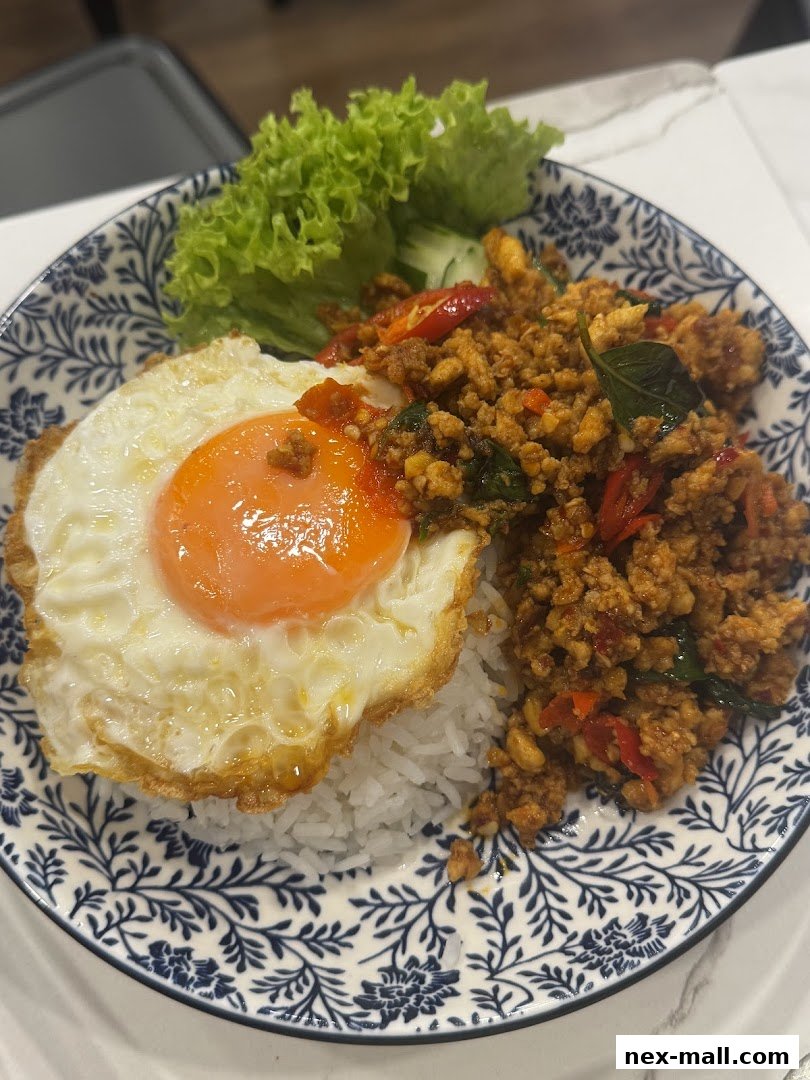A delicious plate of Thai basil chicken with rice and a fried egg, garnished with lettuce and cucumber.