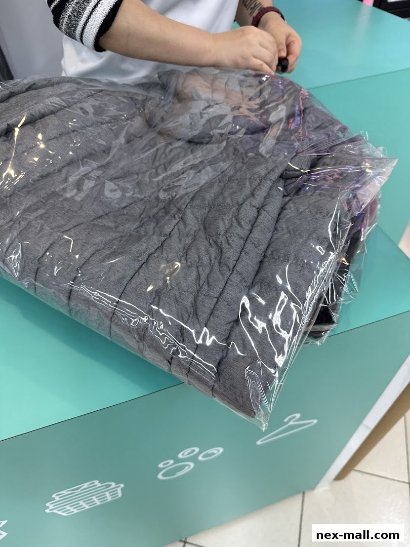 A person is packaging a grey quilted garment in a plastic bag.