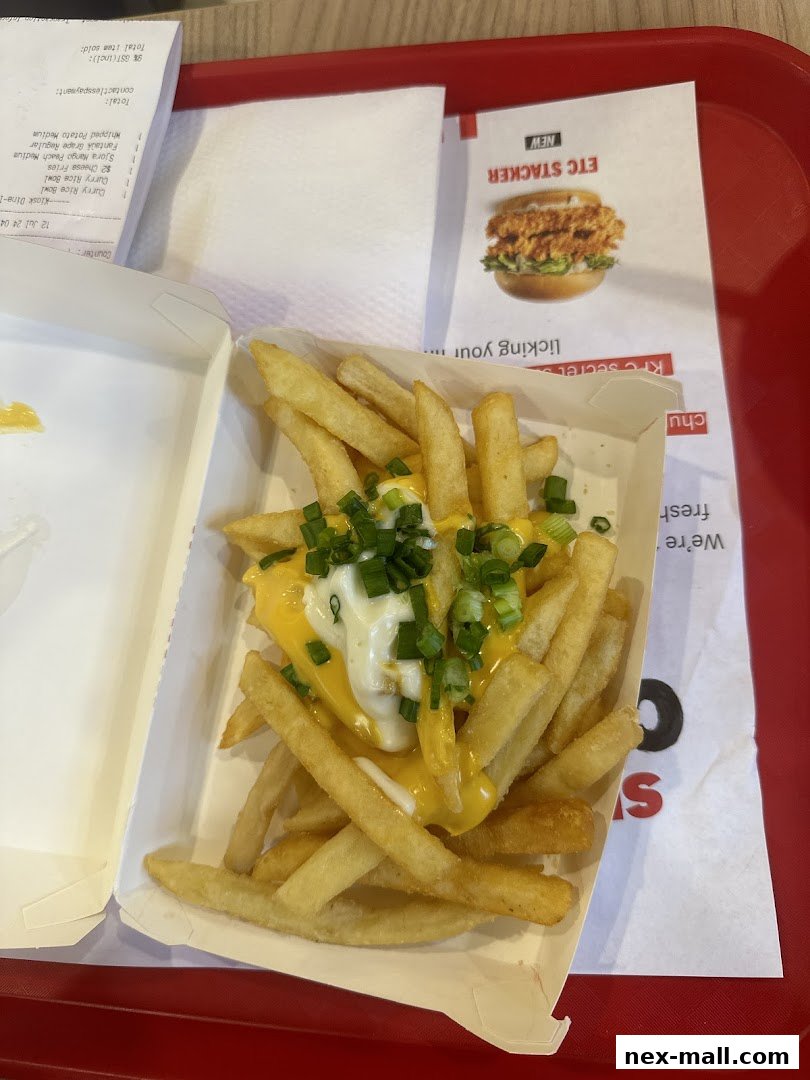 A close-up of KFC's cheese fries topped with green onions and a creamy sauce.