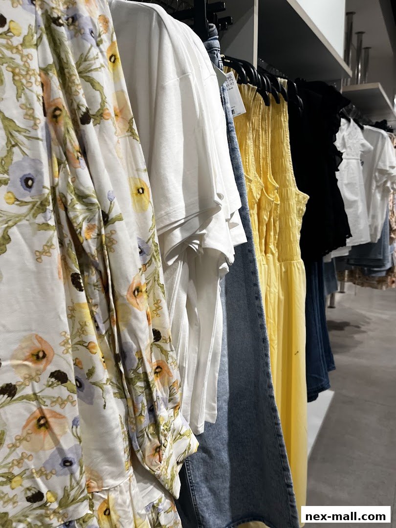 A rack of colorful clothing, including a floral dress, white t-shirts, and a yellow dress.