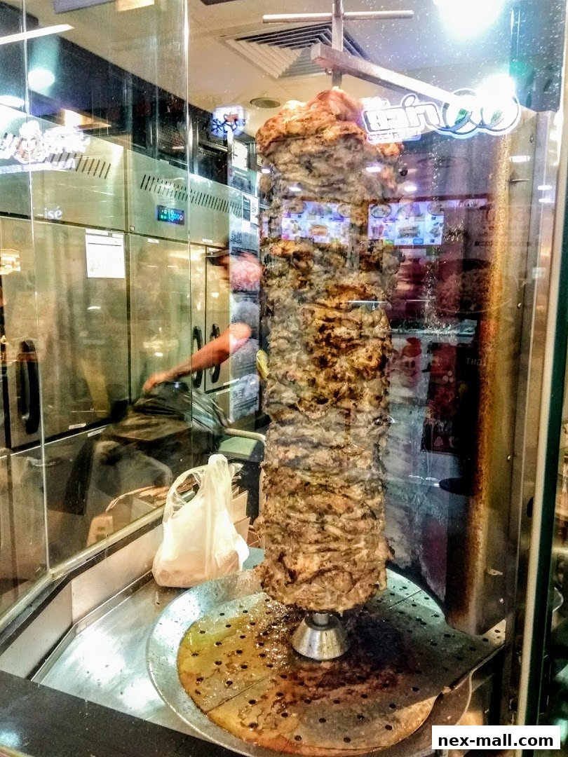 A vertical rotisserie of seasoned meat, likely for shawarma or döner kebab, in a shop window.
