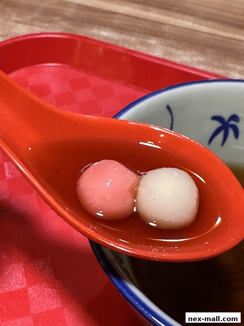 A close-up shot of a spoon holding two sweet dumplings in a light broth.
