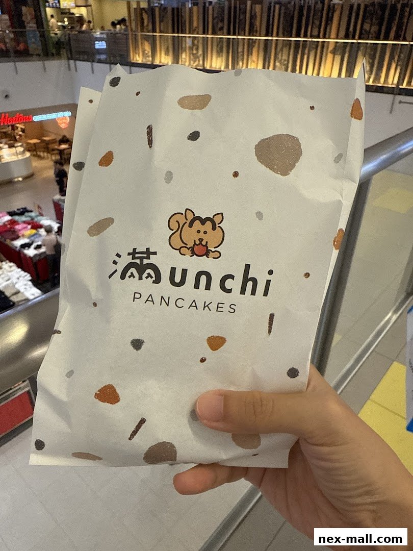 A hand holds a paper bag with the Munchi Pancakes logo and a cute squirrel graphic.