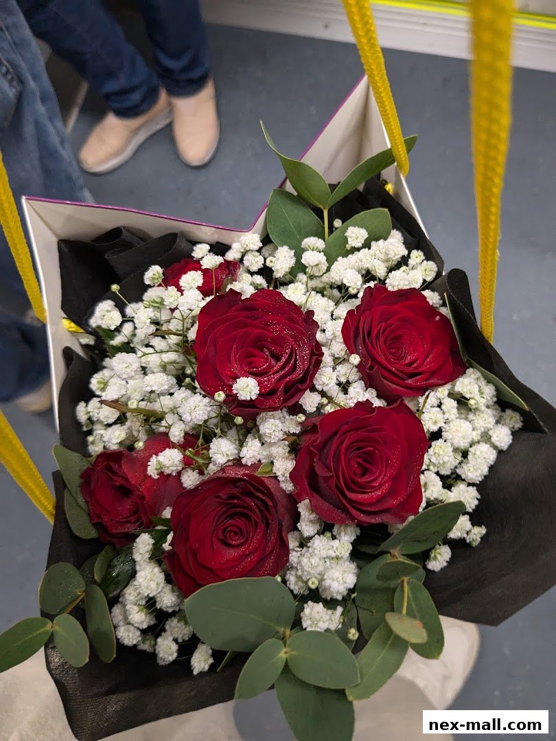 A bouquet of red roses and baby's breath in a box with yellow handles.