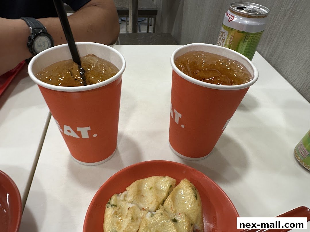 Two orange cups with drinks and ice, a plate of food, and a can on a white table.