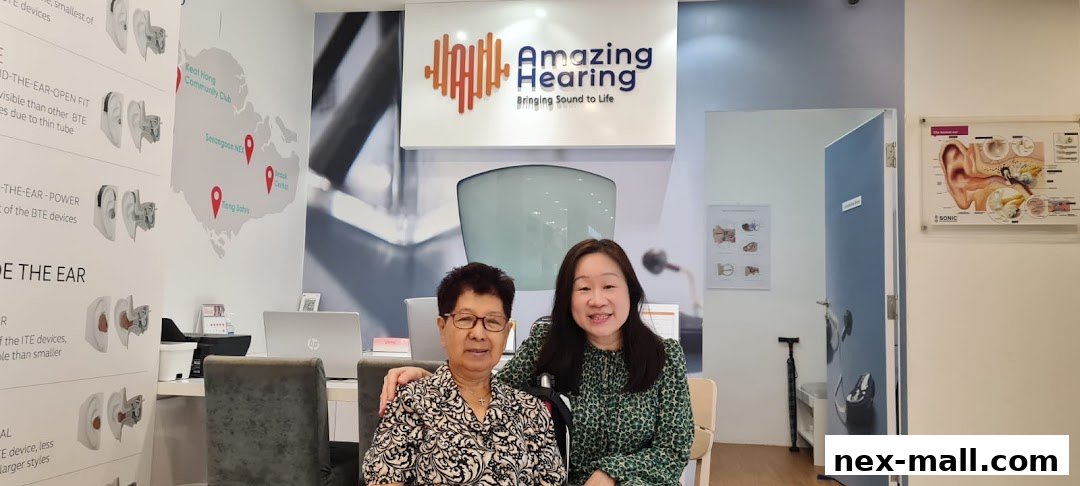 Two women smiling in a hearing aid shop with informational displays on the walls.