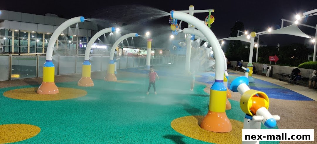 Children playing in a colorful water playground with spray features at night.