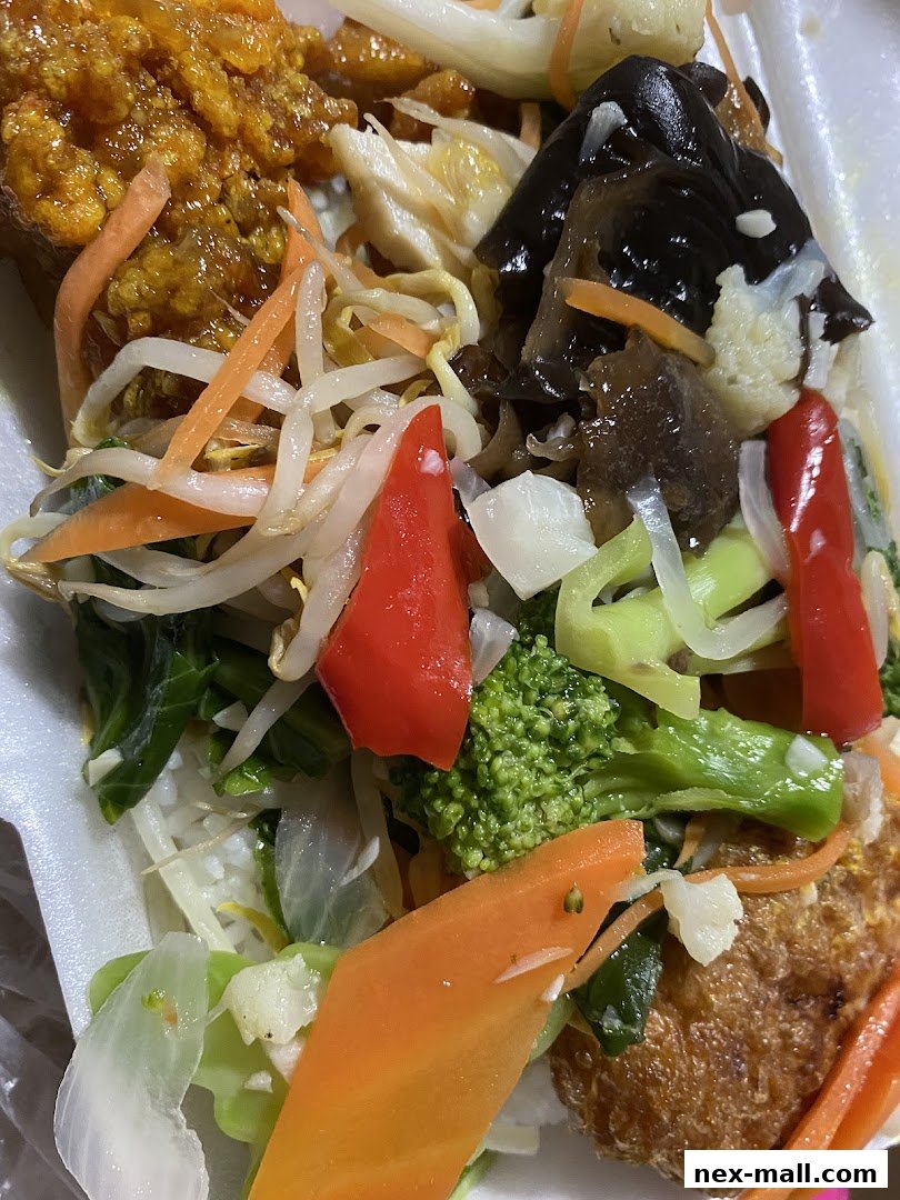 A close-up of a takeout container filled with rice, vegetables, and fried chicken.