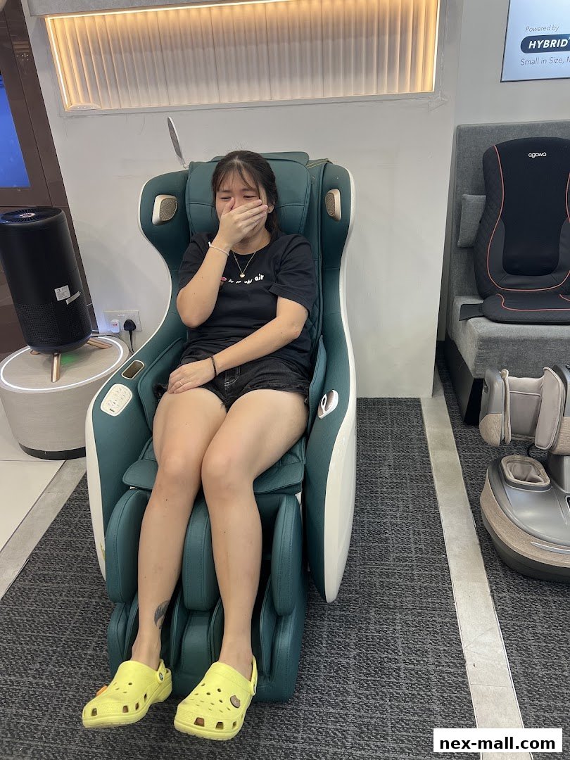 A young woman sits in a massage chair, covering her mouth with her hand.