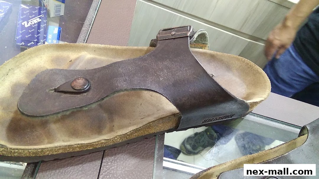 A close-up of a brown leather sandal with a buckle, displayed on a glass surface.