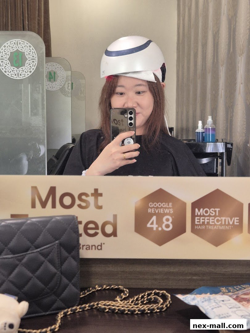 A woman takes a selfie while wearing a hair treatment helmet in a salon.