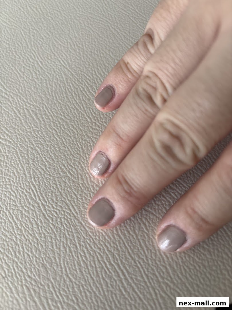 A close-up shot of a hand with neatly painted taupe-colored nails on a textured surface.