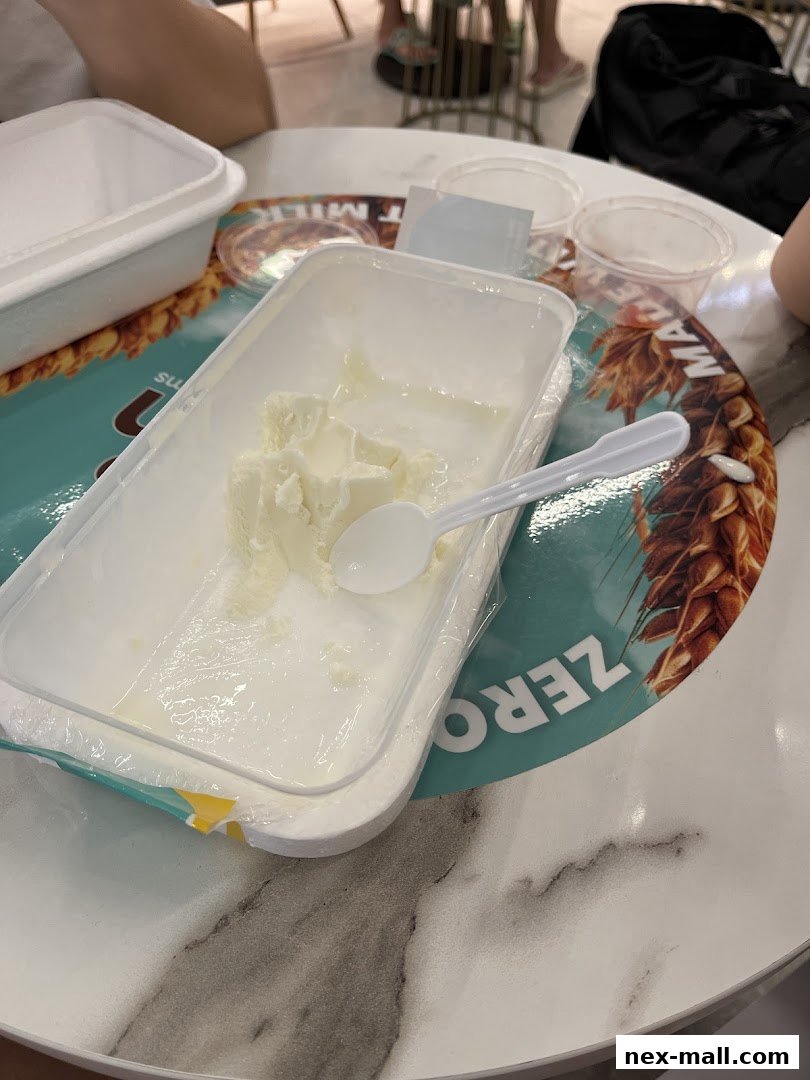 A container of frozen yogurt with a spoon on a table with other containers.