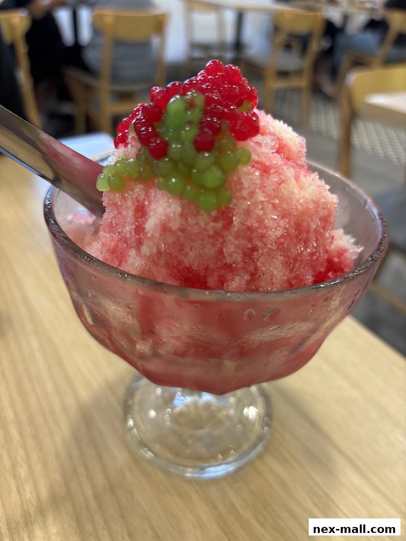 A refreshing bowl of shaved ice dessert topped with red and green jelly balls.