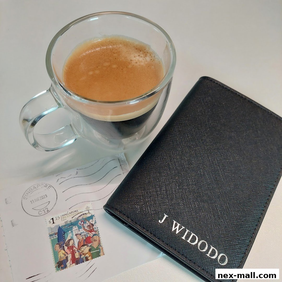 A personalized black passport holder with the name J WIDODO next to a cup of espresso and a stamped envelope.