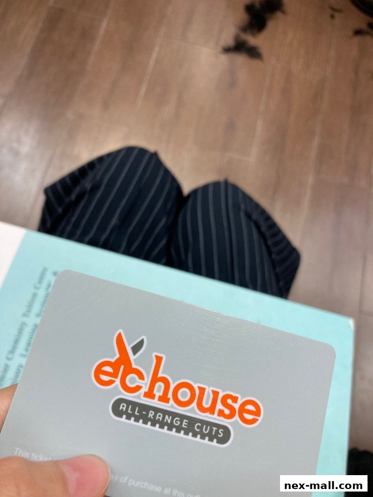 A hand holds a gift card for EC House All Range Cuts over a book and striped pants.