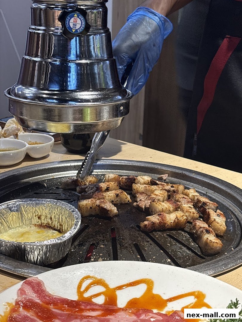 A person grilling pork belly at a Korean BBQ restaurant with a cheese dip.