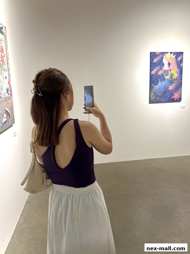 A woman photographs a colorful painting in a brightly lit art gallery.