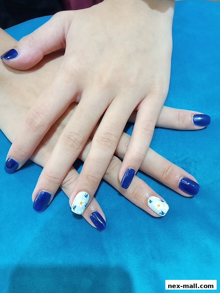 A close-up of hands with beautifully manicured nails, featuring a mix of solid navy blue and white with floral accents.