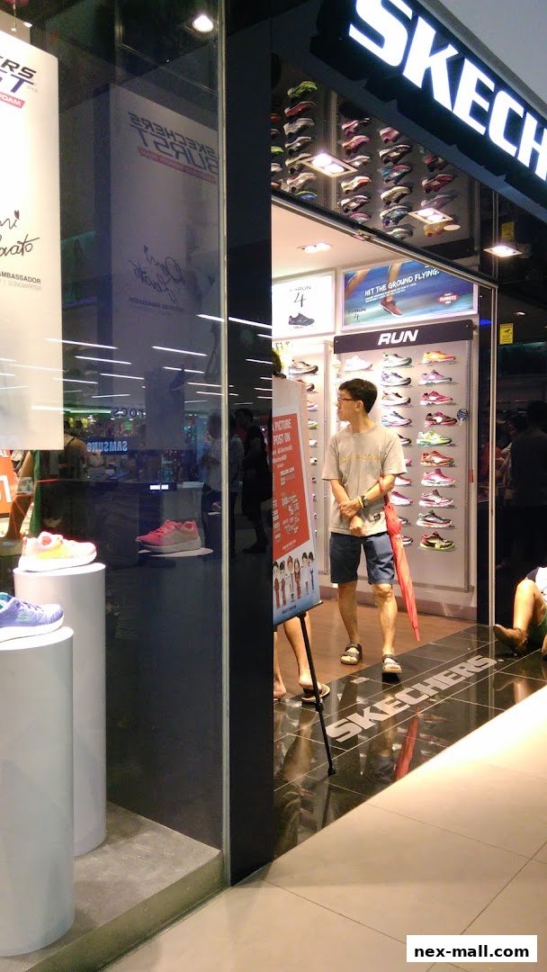 The entrance of a Skechers store showcasing various athletic shoes and a man holding an umbrella.
