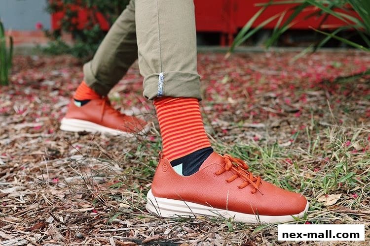 A person wearing stylish orange striped socks and brown leather sneakers walks outdoors.