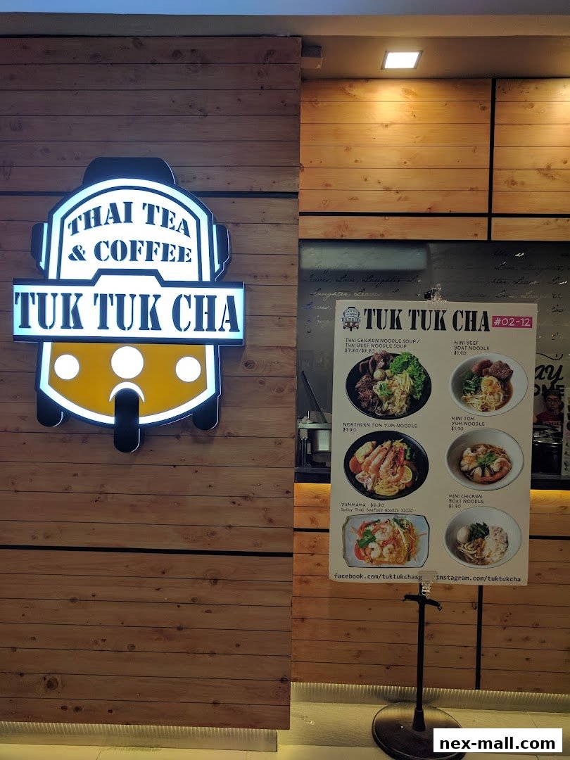 A sign for Tuk Tuk Cha, a Thai tea and coffee shop, with a menu board displaying various noodle dishes.