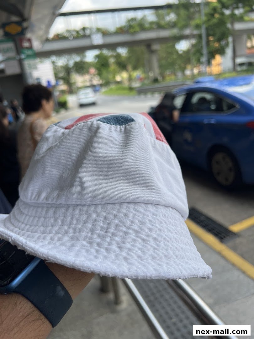 A person holds a white bucket hat with red and blue accents in front of a street scene.