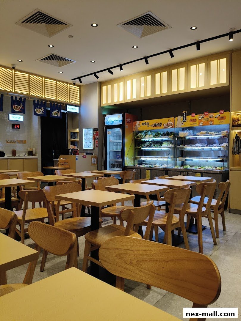 Interior of a Gong Yuan Ma La Tang restaurant with tables, chairs, and a display of fresh ingredients.