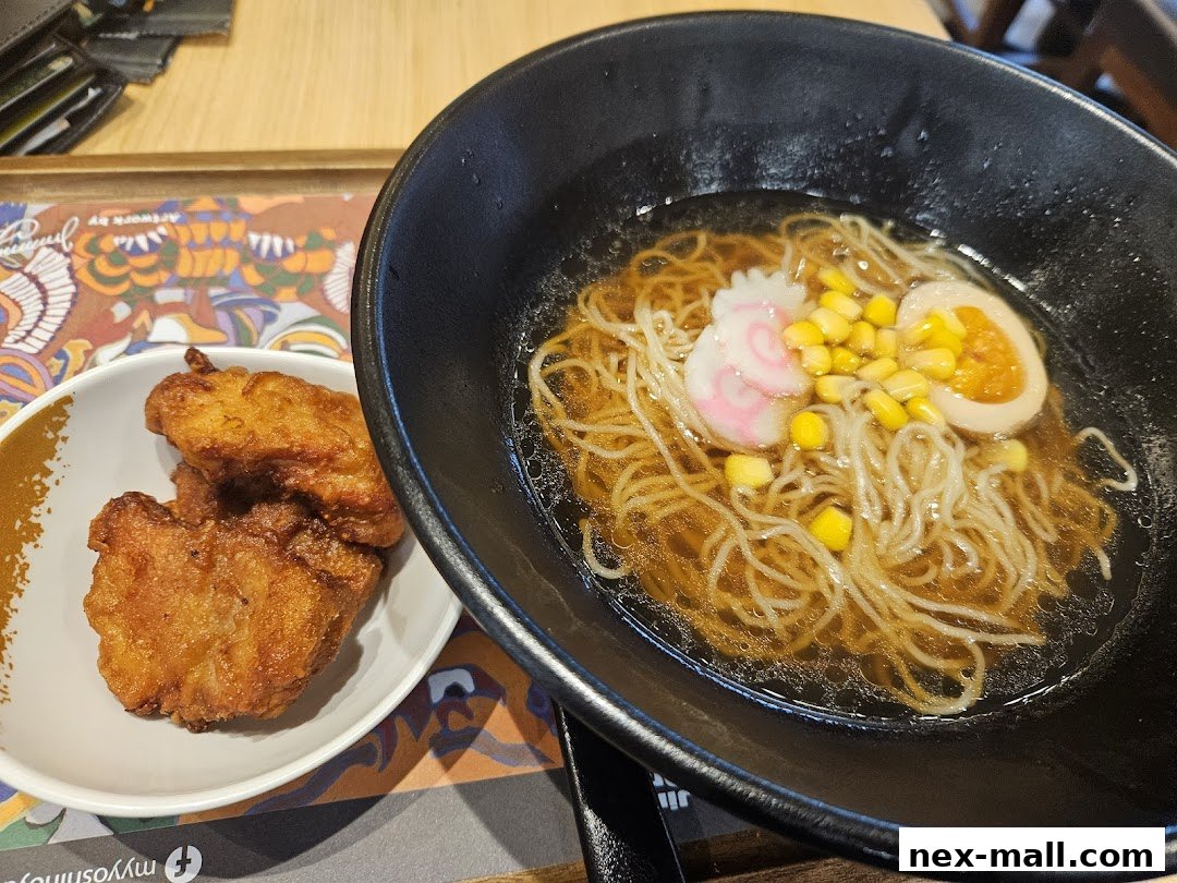 A bowl of ramen with noodles, corn, egg, and fish cake, served with fried chicken.