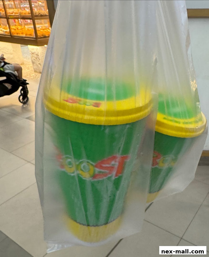 Two green Boost Juice cups with yellow lids are in a plastic bag.