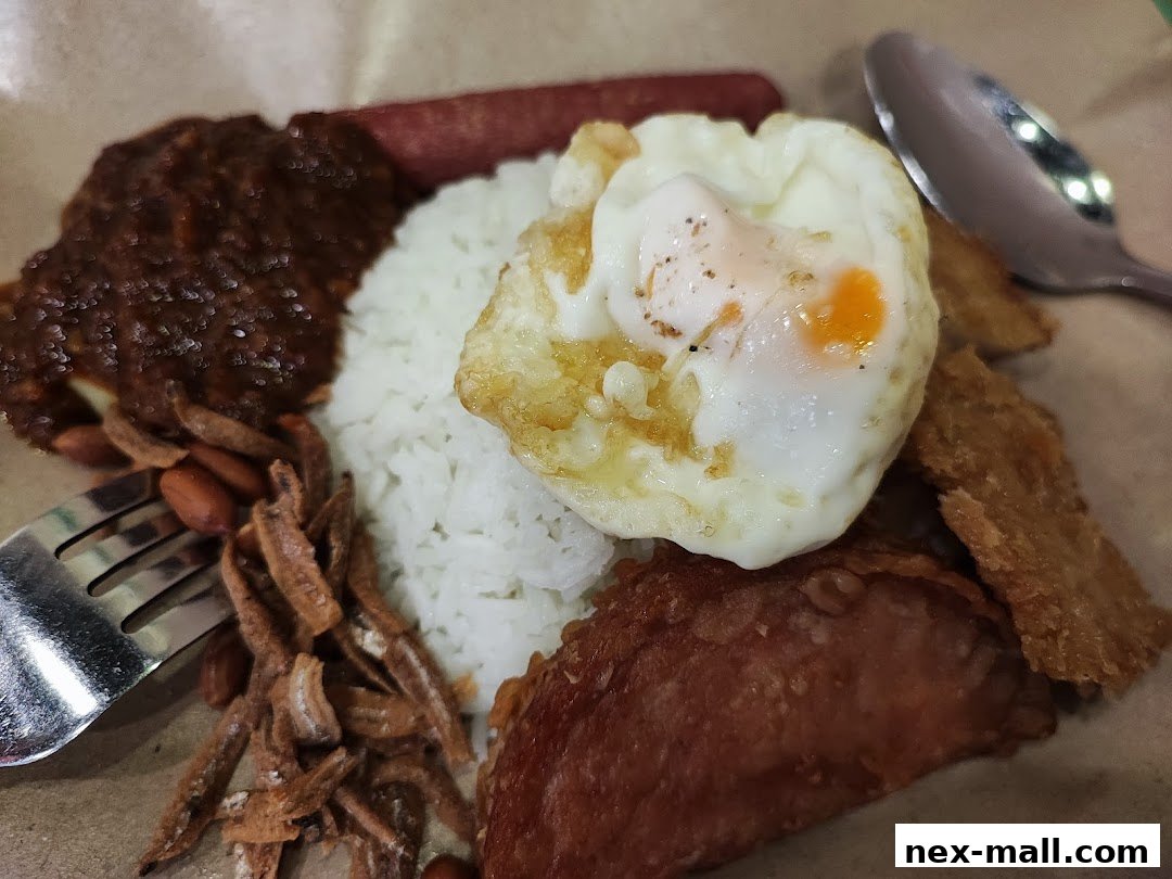 A close-up of a delicious Nasi Lemak dish with fried egg, sambal, anchovies, peanuts, and fried chicken.